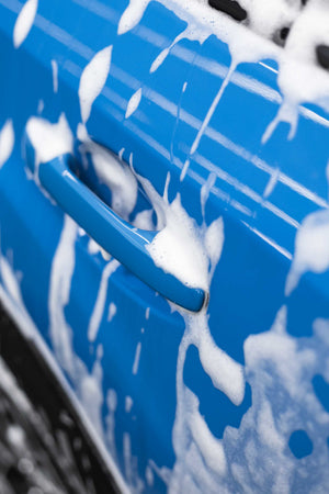 Close-up of a blue car door with soap suds on it.