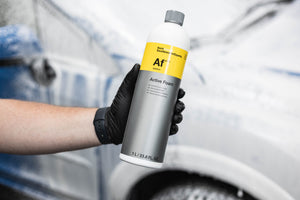 Person holding a bottle of 'Active Foam' car wash product with a blurred car in the background