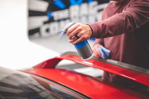 A closeup of someone spraying a car's back window with Koch Chemie glass cleaner.