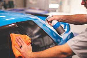 A closeup of someone spraying Koch Chemie glass cleaner on a car's side window.