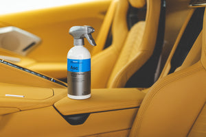 A spray bottle of Koch Chemie surface cleaner propped on the center console of a yellow leather car interior.