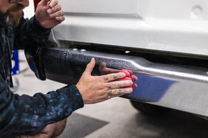Person cleaning a car bumper with a KochChemie Abrasive Clay Bar.