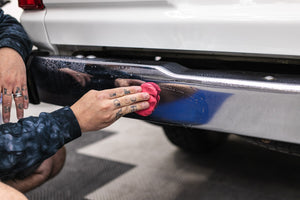 Person cleaning a car bumper with a KochChemie Abrasive Clay Bar.