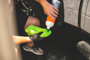 A person pouring a bottle of Koch Chemie Eulex onto a green towel with the background of a white car.