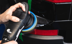A person using a Rupes Polisher on the back of a black vehicle.