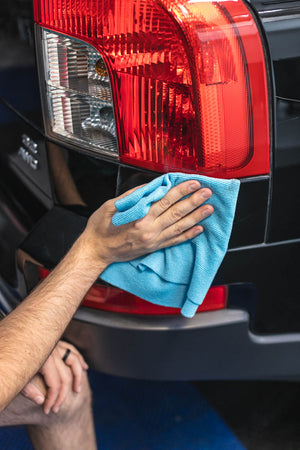 Person cleaning a car's rear tail light with a blue microfiber cloth.