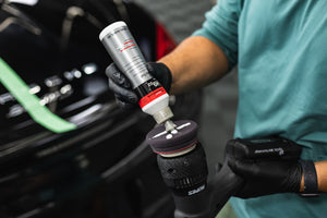 A person pouring KochChemie Heavy Cut onto a KochChemie Heavy Cut Pad v2 76mm attached to a polisher.