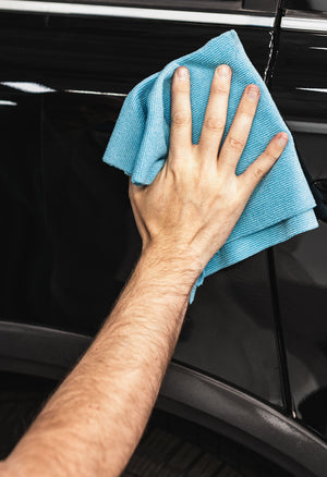 A person using a blue microfiber rag to wipe off a black vehicle.