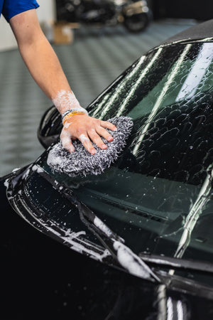 Person washing a black car with a soapy sponge with KochChemie NanoMagic Shampoo on it.