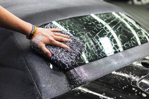 Person cleaning a car window with a microfiber pad