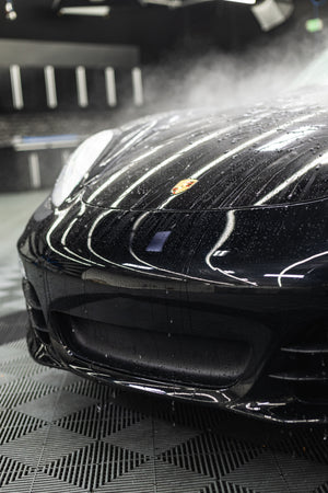 Close-up of a black car's front grille with a visible logo on a textured surface.