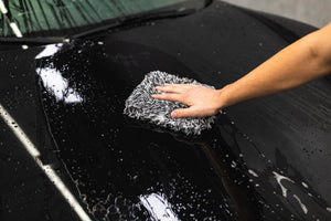Person cleaning a black car with KochChemie NanoMagic Shampoo.