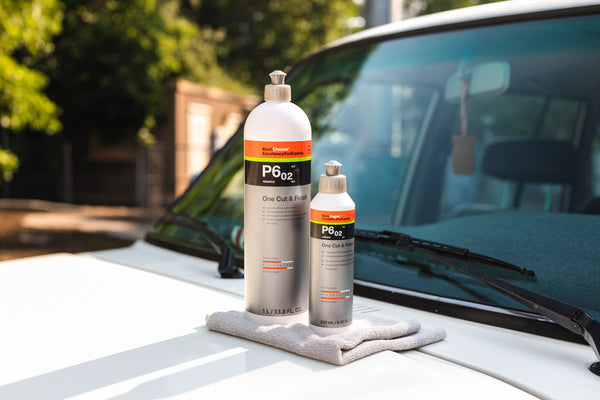 A one liter and 250 milliliter bottle of Koch Chemie One Cut and Finish sitting next to each other on the hood of a white vehicle.