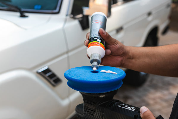 A person squeezing a bottle of Koch Chemie One Cut and Finish on a blue buffing pad.