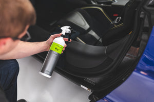 A person holding a spray bottle of Koch Chemie Polstar in front of an open car door.