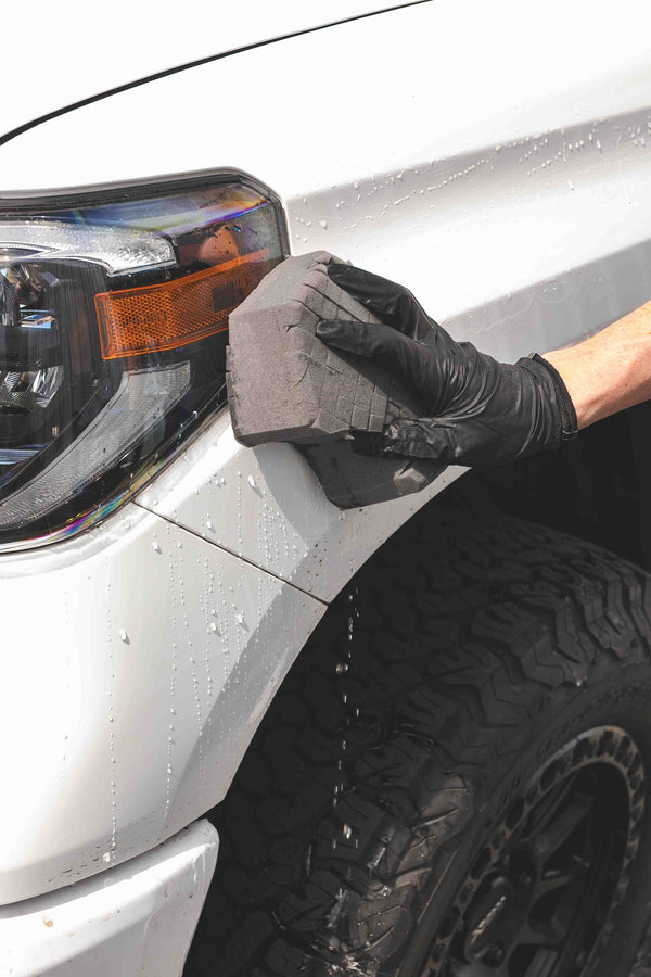 A person cleaning the headlights of a car with an Ultra Safe Sponge.