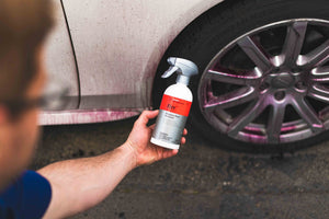 Person holding a bottle of KochChemie Reactive Rust Remover in front of a white car.