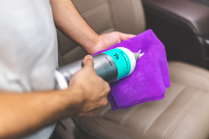 A person pouring Koch Chemie Top Star onto a purple towel with the background of an interior of a car.