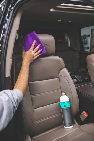 A person cleaning the passenger headrest with a purple towel while a bottle of Koch Chemie top star is in seat. 