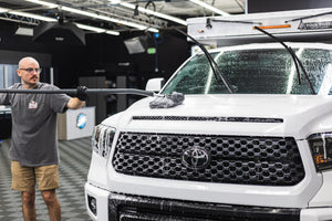 A person cleaning the hood of a truck with a mitt on a stick