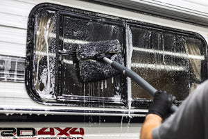 A person cleaning the window of a camper with a mitt on a stick