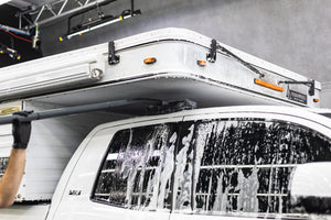 A person cleaning the roof of a truck with a mitt on a stick.