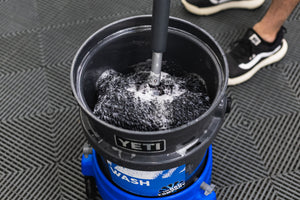 A person dunking a mitt on a stick into a bucket full of soapy water.
