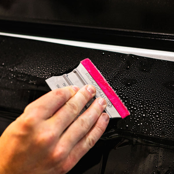 A person using the pink Monkey strip to wipe off liquid from a side door.