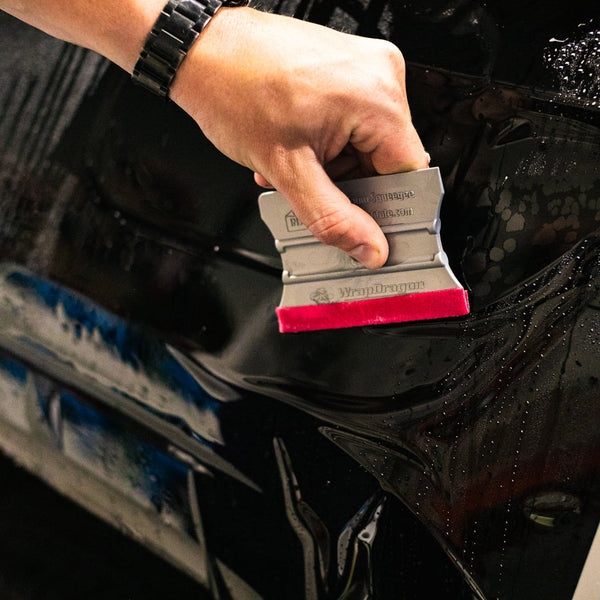 A person using the Yellotools Squeegee to lay black vinyl on a car.