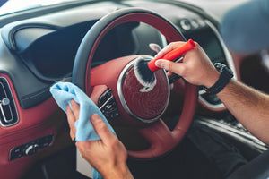 A person scrubbing a marron leather steering wheel with a red synthetic brush.