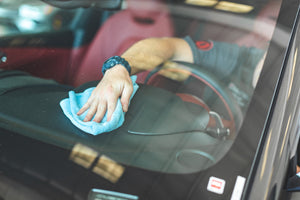 through the front glass a person scrubbing a dashboard with a blue towel.