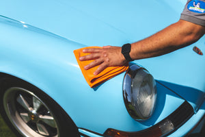 A person drying off a blue classic car with an orange towel.