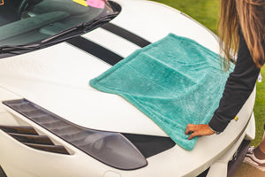 A person laying a teal towel over the hood of a white cars hood.