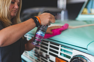 A person spraying a teal car with Dream maker and scrubbing it with a pink towel.