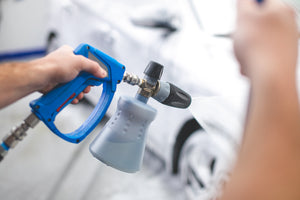 A closeup of a person spraying a white car with a sprayer.