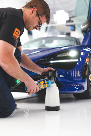 A person pouring Optimum No Wash Rinse into a spray bottle with a blue car in the background.