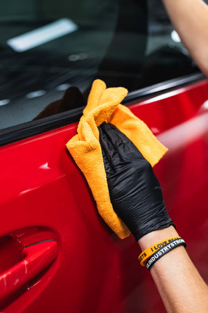 Person cleaning a red car with a yellow microfiber cloth.