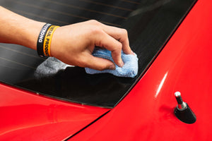 Person cleaning a car window with a blue applicator sponge on a red car.