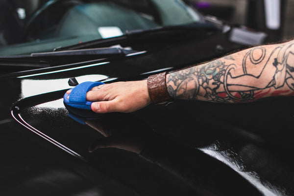 A person applying Optimum Opti Seal to the hood of a black car.