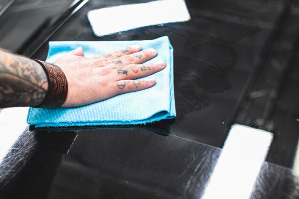 A hand rubbing Optimum Opti Seal on the hood of a car with a blue RIp N' Rag.