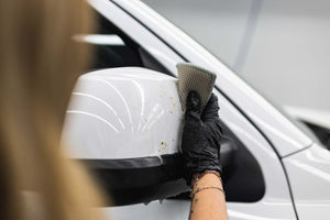 Person cleaning a car side mirror with a Jersey Bug Scrubber.