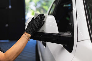Person cleaning a car side mirror with a jersey bug scrubber