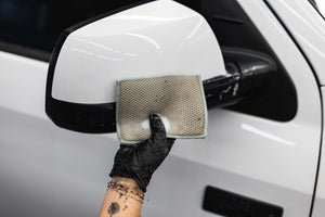 Person cleaning a car side mirror with a jersey scrubber