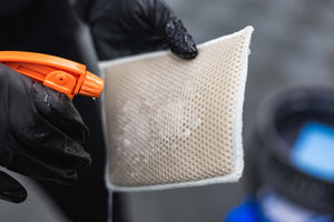 Person wearing black gloves holding a Jersey Bug Scrubber with a spray bottle filled with P&S Bug Off.