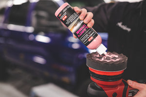Person applying P&S Clarity Creme to a car polisher with a blurred car in the background