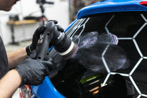 Person using a polisher on a blue car rear window.