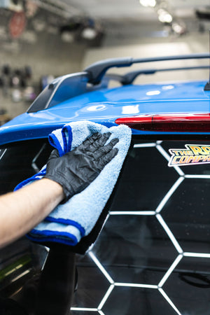 Person cleaning a car rear window with a blue microfiber cloth.