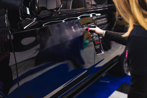 A person spraying P and S defender on the ide of a car.