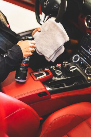 A person spraying an Ice Grey microfiber towel with P&S Inspiration Defender.