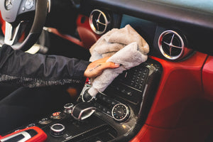 A person wiping the center console of the interior of a vehicle with P&S Inspiration Defender and an Ice Grey microfiber towel.